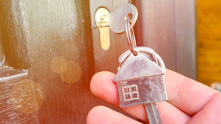 the key in the lock of the front door and a keychain in the form of a house close-up, solar glare, selective focusing, tinted image, the concept of buying and renting real estate, a mortgage symbolの写真素材