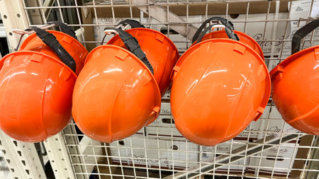 A row of orange safety helmets are hanging on a rack. The helmets are all the same color and appear to be in good conditionのeditorial素材