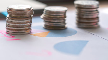 A pile of coins is on top of a piece of paper with a pie chart. The coins are stacked in a pyramid shape, with the largest coin at the bottom and the smallest at the topの写真素材