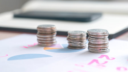 A stack of coins on a table next to a graph. The coins are silver and the graph is pinkの写真素材