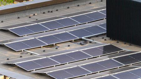A solar panel array is installed on a roof. The panels are black and shiny. The roof is grey
