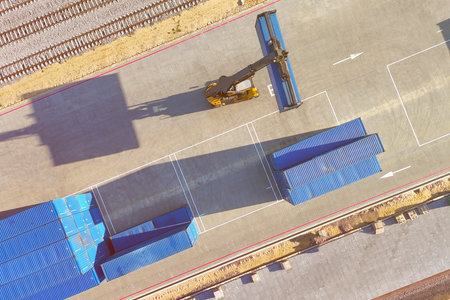 A crane is lifting a container from a train on a railway yard. The crane is mobile and can move...