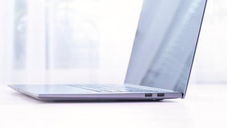 A laptop is open on a table with a window behind it. The laptop is silver and has a keyboardの写真素材