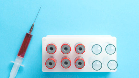 A medical syringe is shown with blood near it, next to test tubes prepared for collecting patients...
