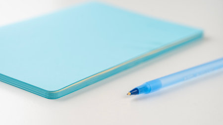 A blue pen rests on top of a blue notebook, both of which are made of paper. The pen is blue and has a small, pointed tip, while the notebook is also blue and has a smooth, glossy surfaceの写真素材