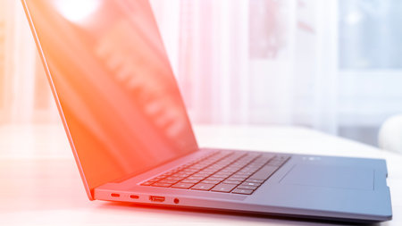 A laptop is open on a table with a red background. The laptop is turned on and the screen is lit up