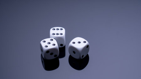 Three white dice are on a dark surface. The dice are arranged in a row, with the middle one slightly larger than the other two. Concept of anticipation and excitementの写真素材