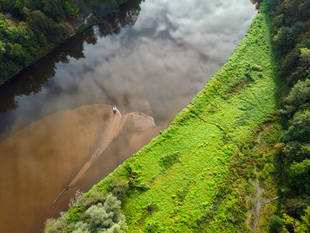 A mesmerizing view from a great height of a deep forest river, photo from a drone. Wild untouched nature, bright green grass on the banks of a beautiful river. Juicy colors in the photo of the river. A river with a green bank and a person in the water.の写真素材