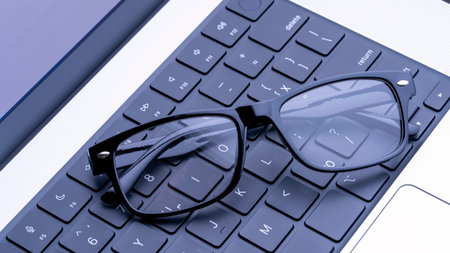 Elegant spectacles perch on a laptop keyboard, serving as a crucial safeguard for the eyes during...