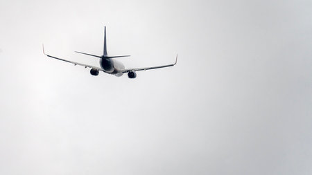 A plane is flying through a cloudy sky. The sky is mostly gray, with a few white clouds scattered...
