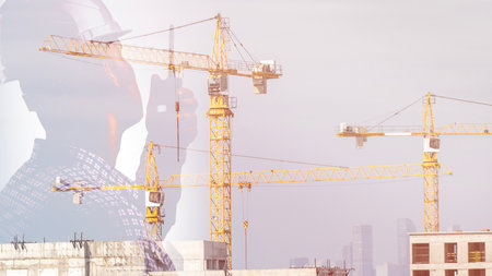 A construction worker in safety gear is seen giving instructions on a walkie-talkie against a backdrop of a construction site with construction cranes. They are responsible for organizing the production process and overseeing the progress of work at the site. The worker is isolated on a white background and looks into the distance, while construction engineers meet to discuss the project on-site. High quality photoの写真素材