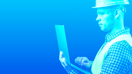 A construction professional, utilizing a laptop on a uniform backdrop. The engineer is seated at his laptop. High quality photoの写真素材