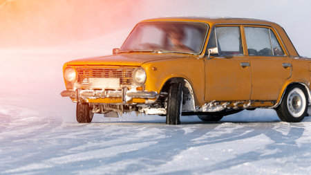 A yellow car is driving along a snowy road. The vehicle is old and covered in rust. The snow covers the ground, and the car leaves a trail behind. The scene is peaceful and quiet. High quality photoの写真素材