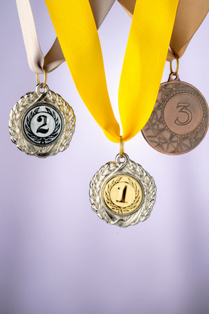 Three medals are hanging on a ribbon, with the middle one being a silver medal with a number 1 on it