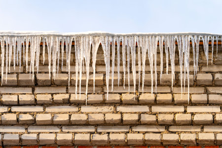 Icicles brick roof. Icicles on the roof in winter, thaw. Beautiful icicles on a winter roof in close-up. High quality photoの写真素材