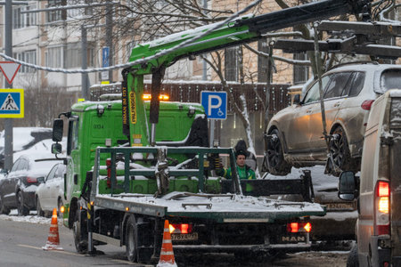 Moscow, January 20, 2026, A green tow truck is pulling a car out of the snow. A man is sitting in...