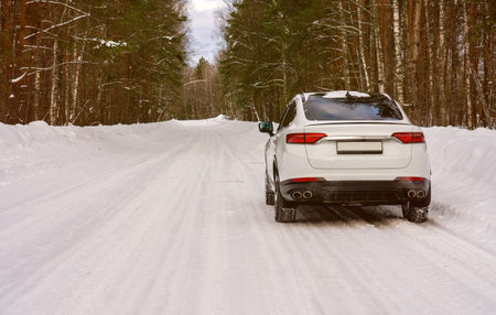 White SUV drives through snowy forest trail. Trees stand tall, covered in winter snow. Road glistens...