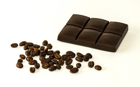 On a light background is dark chocolate tiles and scattered grains of coffeeの写真素材