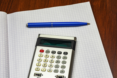 Calculator and blue ballpoint pen lie on a sheet of paper into the cell from a notebook for recordsの写真素材