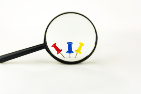 Three drawing pins of different color are visible through a magnifying glassの写真素材