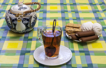 On the table mishandled colored tablecloth. On the tablecloth is a glass cup with tea, tea and sweets in the basket areの写真素材