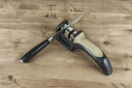 On the wooden surface there is a sharpener and a metal knife with a plastic handle