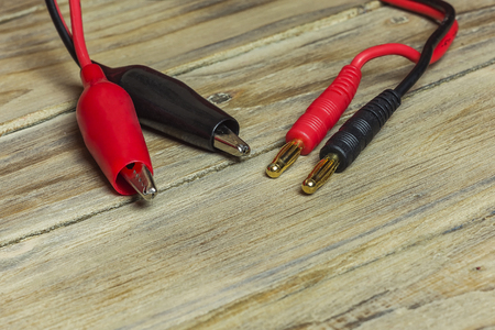 On the wooden surface is a red and black wire with contacts like tulip and crocodile