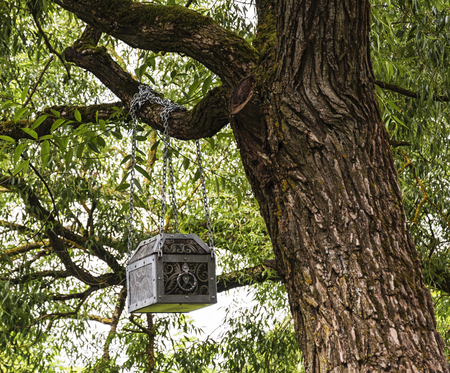 On a branch of a large tree on chains there is a large metal trunkの写真素材