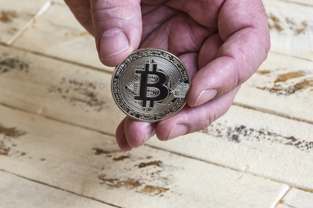 Against the background of the wooden surface of the man's hand holding a silver coin bitcoinの写真素材