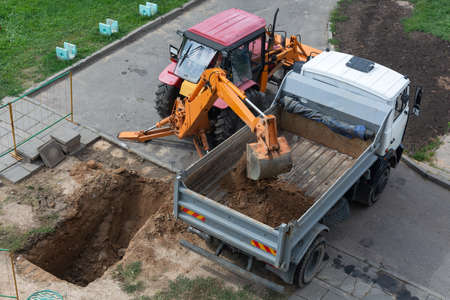Belarus, Minsk-15.08.2018: Tractor with bucket excavator digs a hole and loads the earth into the...
