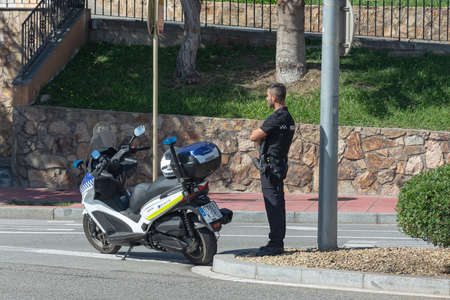 Lloret De Mar, Spain - 10/04/2019: Police officer with a motorcycle at the intersection of a city street. Stock photo.のeditorial素材