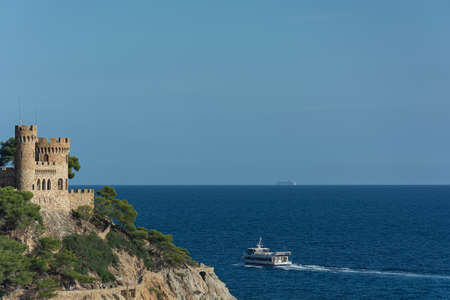 Lloret De Mar, Spain - 09/28/2019: Seascape. An old castle and a ship sailing away into the distance. Stock photoのeditorial素材