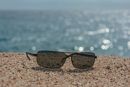 Dark sunglasses on the sand against the sea. blurred background with bokeh elements. Stock Photoの写真素材