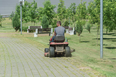 A man drives a lawn mower and drives along the sidewalk, Blurred background. Stock photography.の写真素材