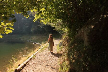 Autumn 2019: Caucasian woman contemplates the reflections on an alpine lake along a trekking pathの写真素材