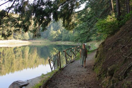 Autumn 2019: Caucasian woman contemplates the reflections on an alpine lake along a trekking pathの写真素材