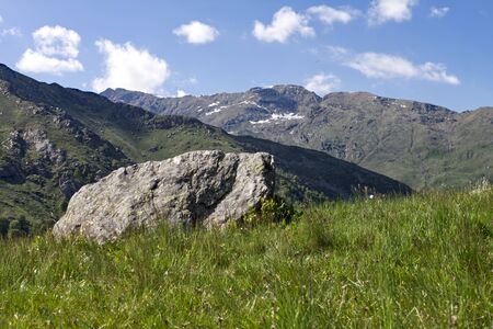 a large granite stone resting on a meadow with the alps in the backgroundの写真素材