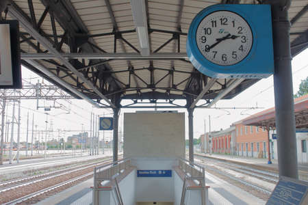 train station, italy - summer 2020: a big blue clock over the binary near the exit in train stationの写真素材