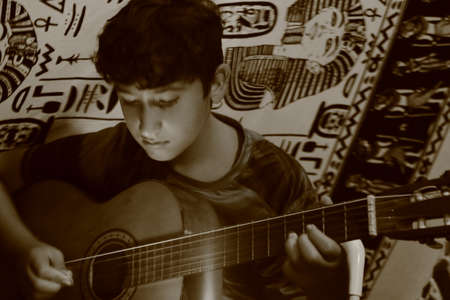 A caucasian boy plays guitar by during an evening camping on the beach