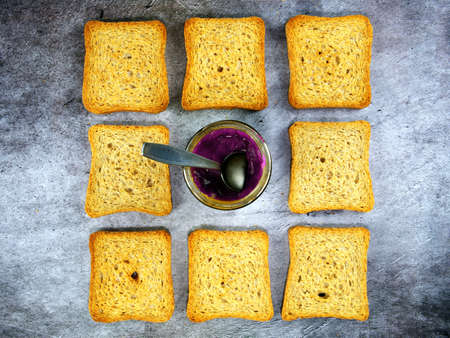 Flat lay of teaspoon dipped in a jar of grape jelly with rusks around
