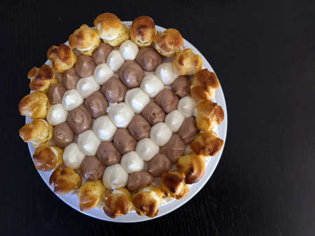flat lay photo of a saint honore cake on a white plate resting on a black wood table