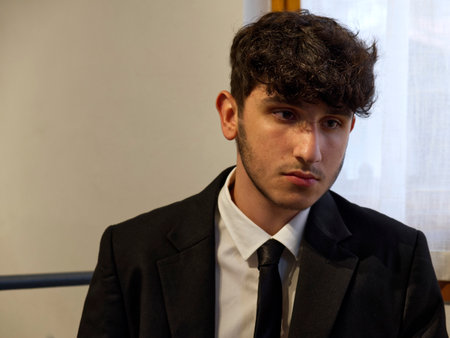 a sitted caucasian teenager in a business suit adjusts his white shirtの写真素材