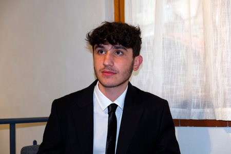 a sitted caucasian teenager in a business suit adjusts his white shirtの写真素材