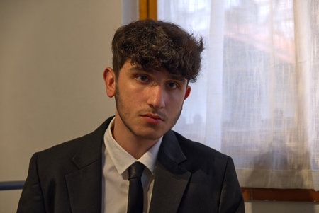 a sitted caucasian teenager in a business suit adjusts his white shirtの写真素材