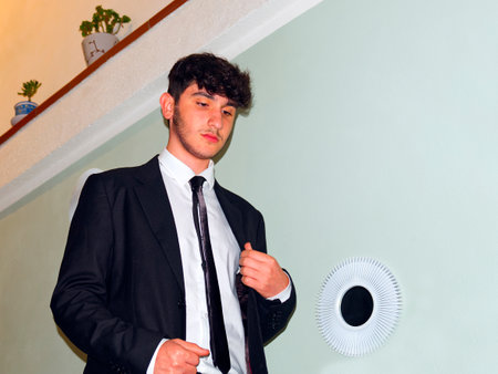 a caucasian teenager goes down the stairs in a business suit adjusts his white shirtの写真素材