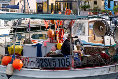 Savona, Italy - 7 apr 2024: a fisherman mends fishing nets on his fishing boatのeditorial素材