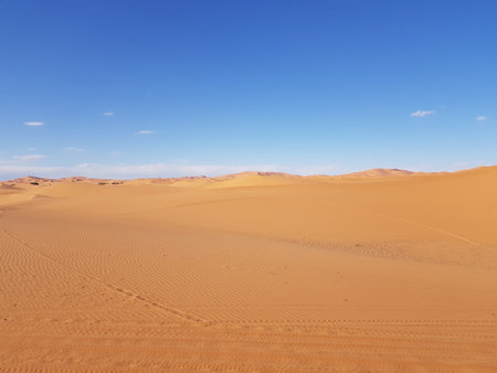A desert landscape with a blue sky and footprints in the sandの写真素材