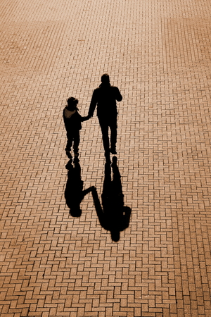 Silhouette and shadows of  man and child holding hands on a footpath made of bricksの写真素材