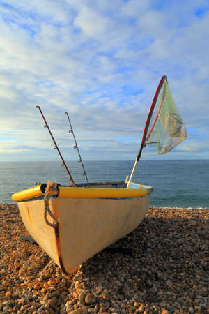 Small fishing boat with rods and net on the pebbles beach near village of Beer, Devonの写真素材