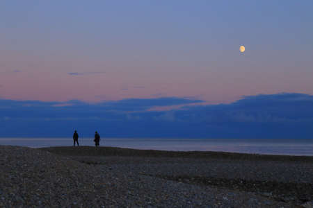 Silhouettes of people walking on the pebbles beachの写真素材